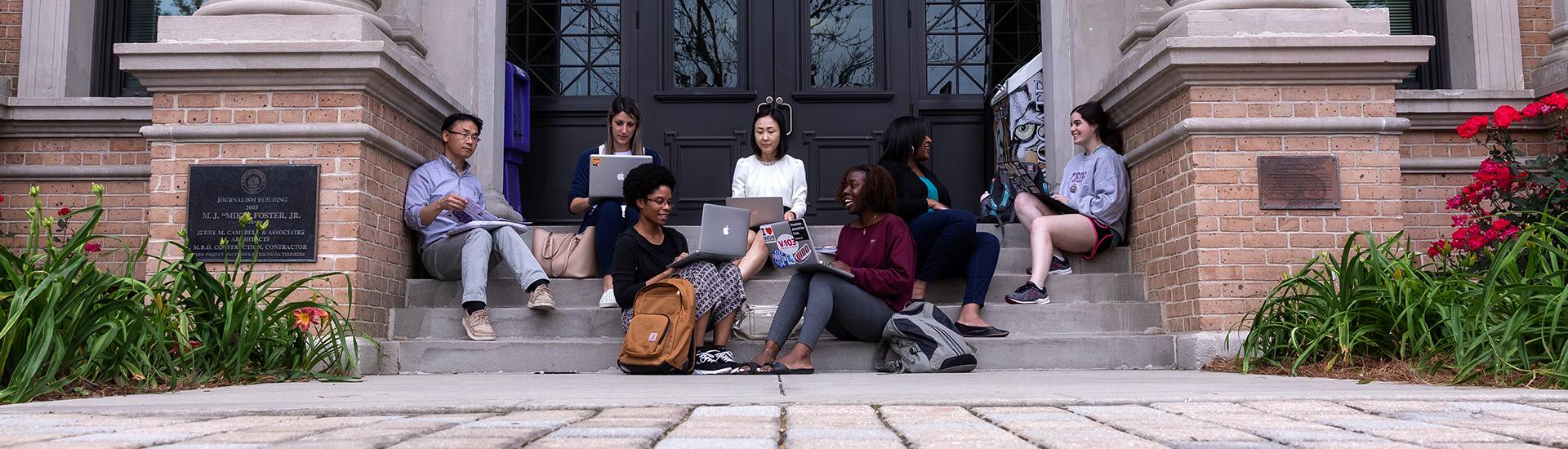Professors and students on computers outside of the  Journalism building